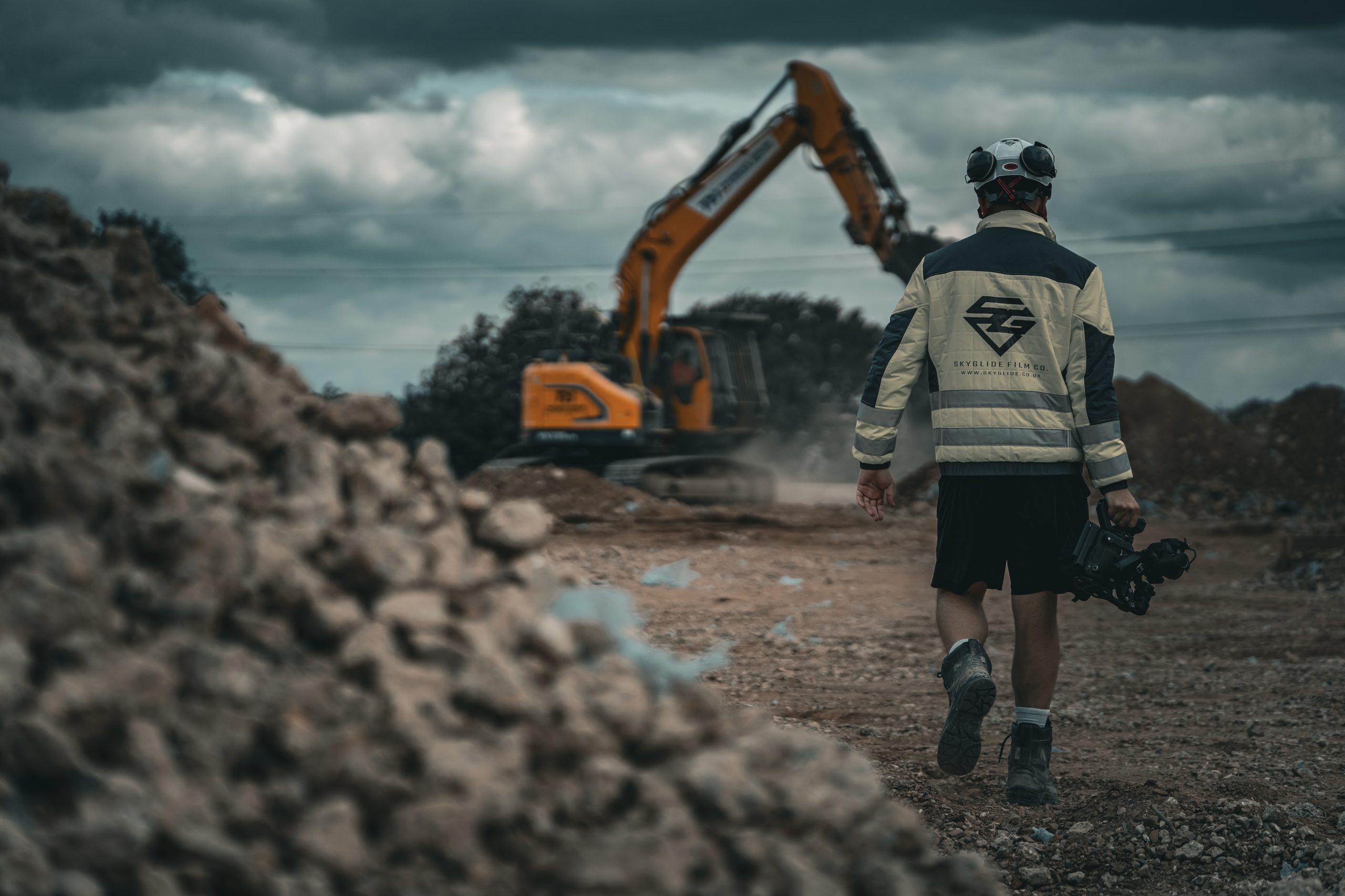 SkyGlide camera operator walking onto a live construction site towards an excavator