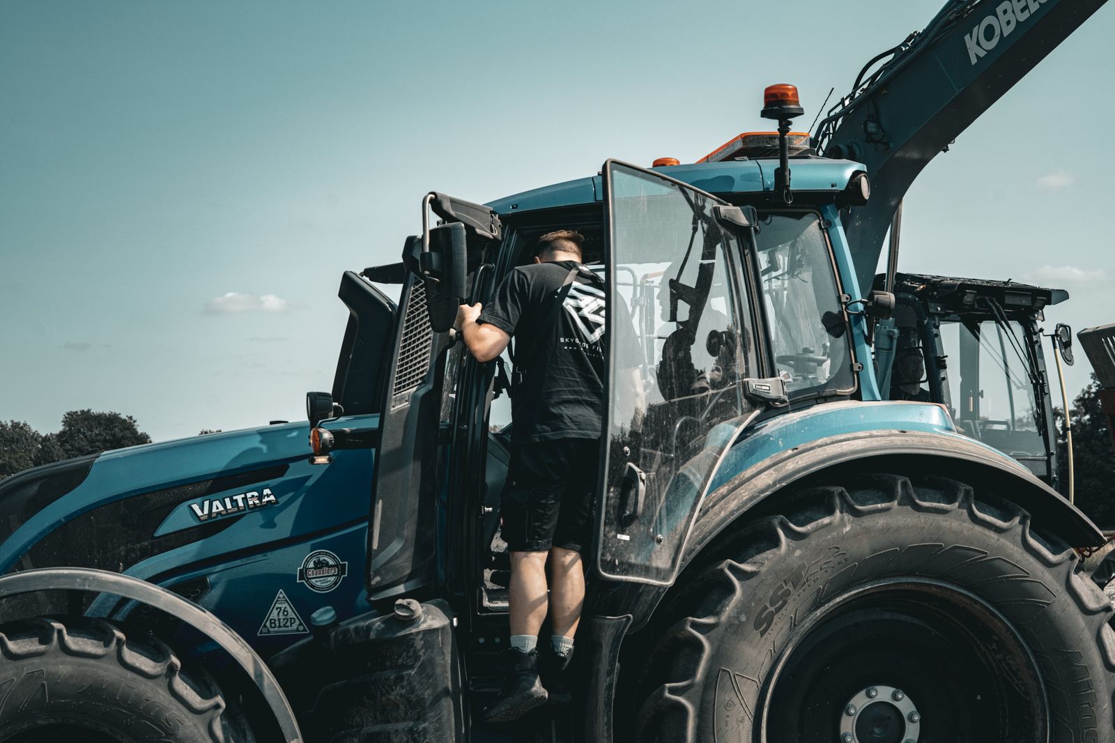 Crew boarding a Valtra tractor with a Kobelco excavator working behind
